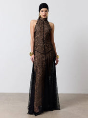 Model wearing a black high-neck sleeveless lace maxi dress on a plain backdrop, styled with statement jewelry for an evening look.