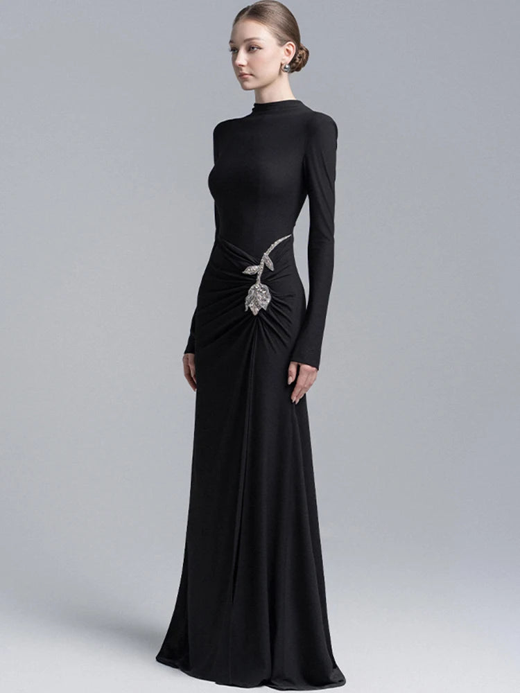 Full-length view of a black floor-length gown with sleek sleeves and asymmetric drape across the skirt, creating a refined formal silhouette