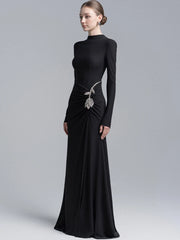Full-length view of a black floor-length gown with sleek sleeves and asymmetric drape across the skirt, creating a refined formal silhouette