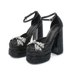 Pair of black platform block-heel sandals on a white background with pearl bow embellishments and ankle straps for a dressy finish.