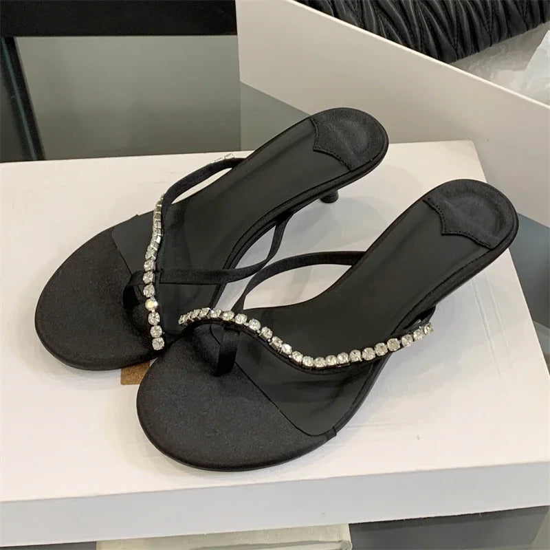Black sandals with crystal embellishments on a white surface
