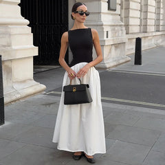 Woman in a sleeveless black and white maxi dress holding handbag on a city street