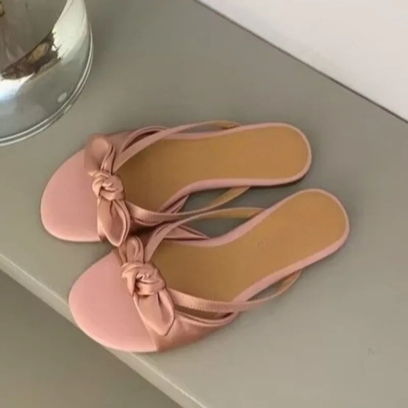 Blush bow open-toe sandals paired for work and spring occasions, a pair of pink sandals with a bow on a light grey surface