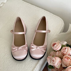 Pair of blush pink Mary Jane pumps with bows beside roses