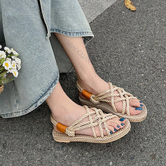 Person wearing braided sandals on a pavement with a floral arrangement.