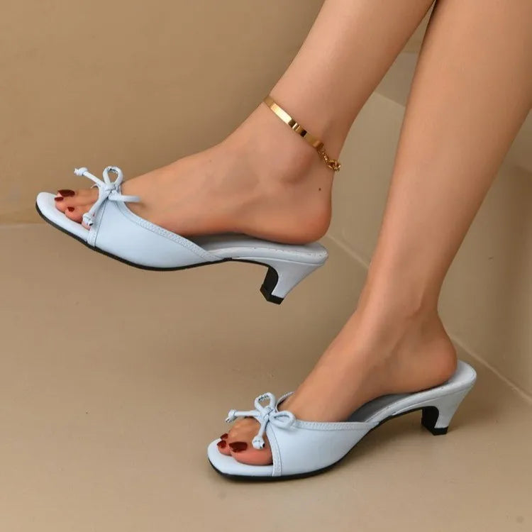 White high-heeled shoes worn by a person on a beige background