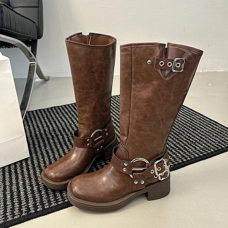 Brown square-toe block heel boots with adjustable buckles are styled on a textured mat.