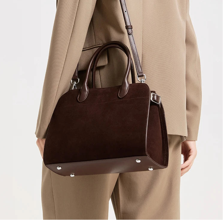 Side angle showing the zipper closure and strap attachment on a brown suede shoulder bag with a refined, minimal profile.