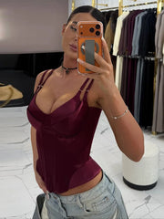 Styled outfit pairing a burgundy satin corset top with relaxed jeans, creating a polished night-out look in a minimal indoor setting.