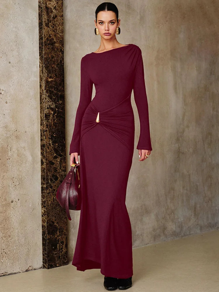 A Woman wearing a burgundy ruched long-sleeve maxi dress styled for an autumn party against a textured wall.