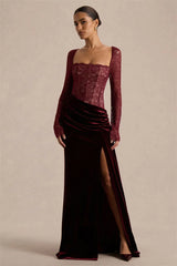 Side-front angle highlighting the high slit and draped velvet skirt on a burgundy square-neck maxi dress styled for formal evenings.