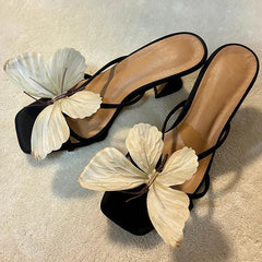 Black high-heeled sandals with butterfly decorations on a light background
