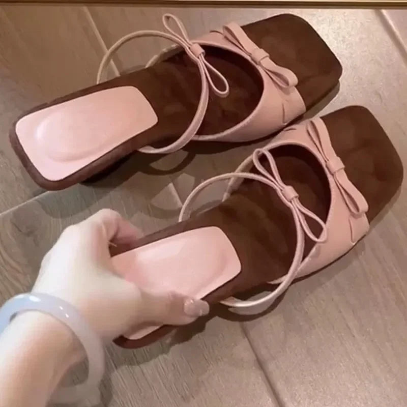 Pair of pink and brown sandals held by a hand on a wooden floor.