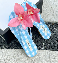 Blue checkered flip-flops with pink flowers on a gray surface