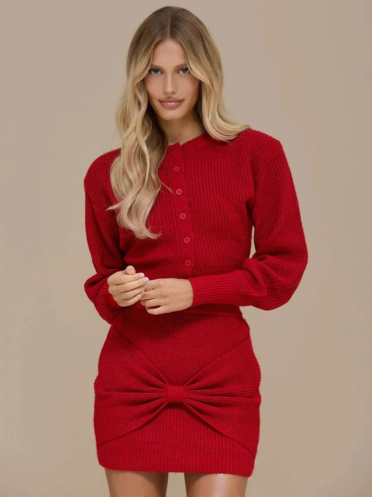 Studio front view of a red knit two-piece set with a button-front long-sleeve top and a mini skirt with bow twist detail.