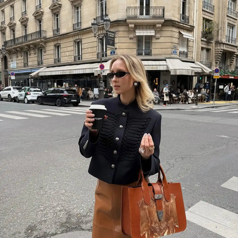 Outfit view of a black braided-trim cropped jacket worn open with denim, highlighting the waist-length cut and sharp silhouette.