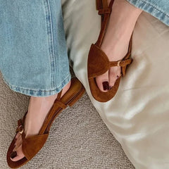 Brown sandals worn with light blue jeans on a neutral background