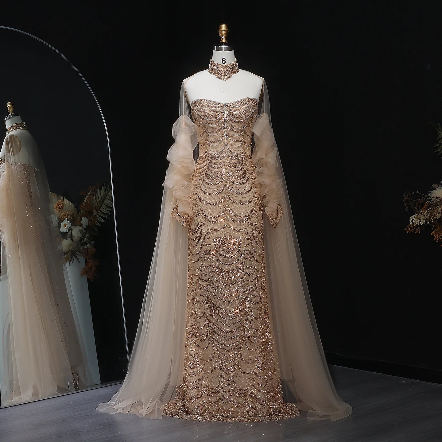 Elegant evening gown with sheer sleeves on a mannequin against a dark background