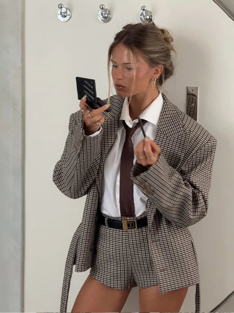 Mirror selfie showing a checkered blazer and matching shorts set, styled with a white shirt, slim tie, and minimal accessories.