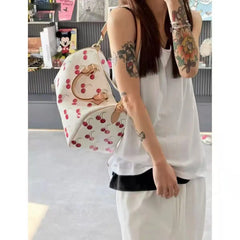 A person holding a Woman holding a barrel-shaped cherry print handbag with top handles in an indoor setting.