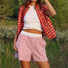 Person wearing a red polka dot shirt over a white top and pink shorts in a natural setting.