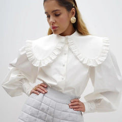 A woman modeling a white chiffon V-neck shirt with pleated details.