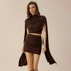 Model wearing a chocolate-brown draped shawl top with scarf detail and matching fitted mini skirt on a neutral background.