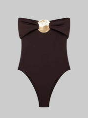 Dark brown off-shoulder bodysuit on a light background, featuring a folded neckline and a central gold-toned metal accent at the bust
