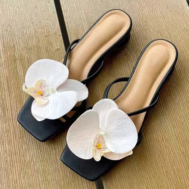 Black sandals with white orchids on a wooden surface