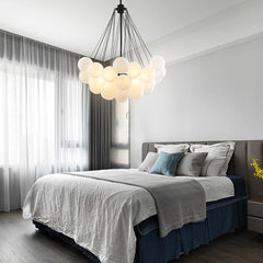 A frosted glass chandelier with a silver iron finish hanging from the ceiling of a bed room. The chandelier has a white color, and it appears to be dimly lit, enhancing the cozy ambiance of the room.