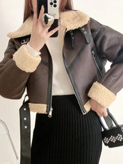 A person holding a smartphone in front of their face, wearing a Coffee colored faux leather fur short jacket with a belt, paired with a white top and a black skirt.