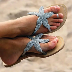 Starfish-shaped sandals with rhinestones worn on feet against a blurred natural background