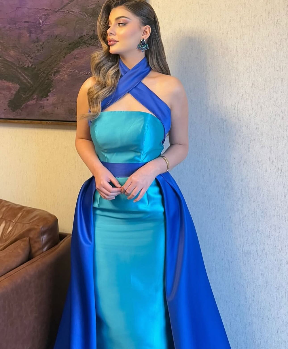 Indoor full-length view of a blue and turquoise satin halter gown with a sleek mermaid fit and dramatic contrast drape.