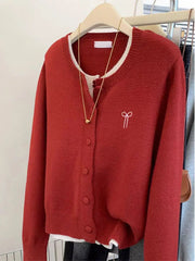 Red sweater with a white bow design on a hanger against a neutral background