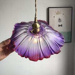 A pendant LED light fixture with a lavender glass shade and a knob switch,  hanging with a painting lon the  back ground.