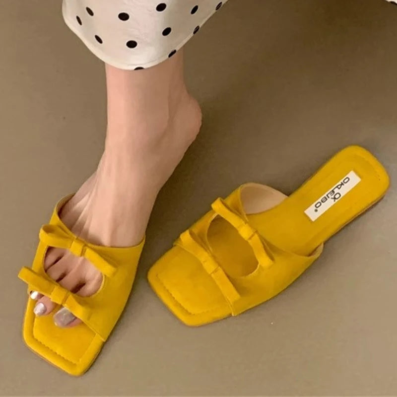 Cozy elegant outdoor flat sandals displayed for summer events yellow sandals with a brand label worn by a person on a beige background