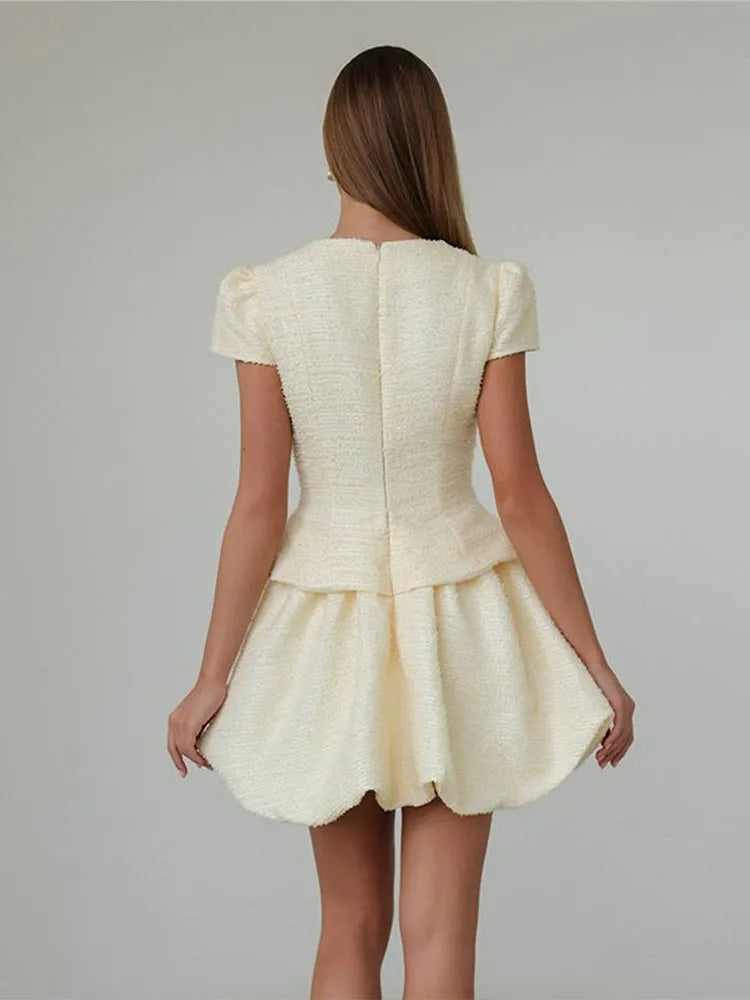 Back look of a cream tweed co-ord set with short sleeves and a structured mini skirt, creating a polished office-ready silhouette.