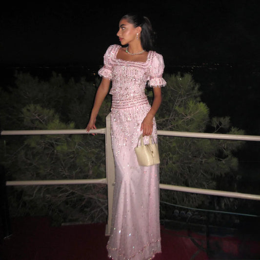 Close-up of the pink square-neck bodice showing crystal beading, textured trim, and refined detailing under warm indoor lighting.