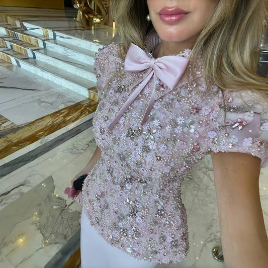Close view of the pink round-neck top highlighting crystal beading and sequin sparkle across the bodice under soft indoor lighting.