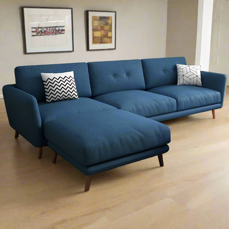 A blue fabric sofa with a chaise on the left side, featuring a modern design with button tufting and wooden legs, with two accent pillows on the sofa.