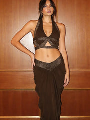 Full look of a brown cutout two-piece evening set styled outdoors near columns, with a slim silhouette and fluid skirt movement.