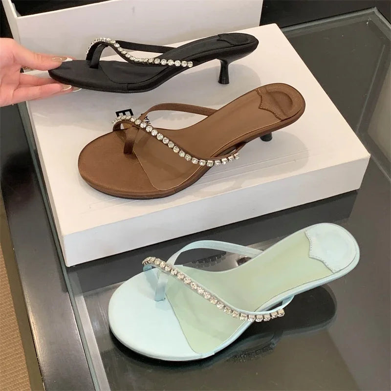 Three pairs of sandals with decorative straps on a reflective surface.