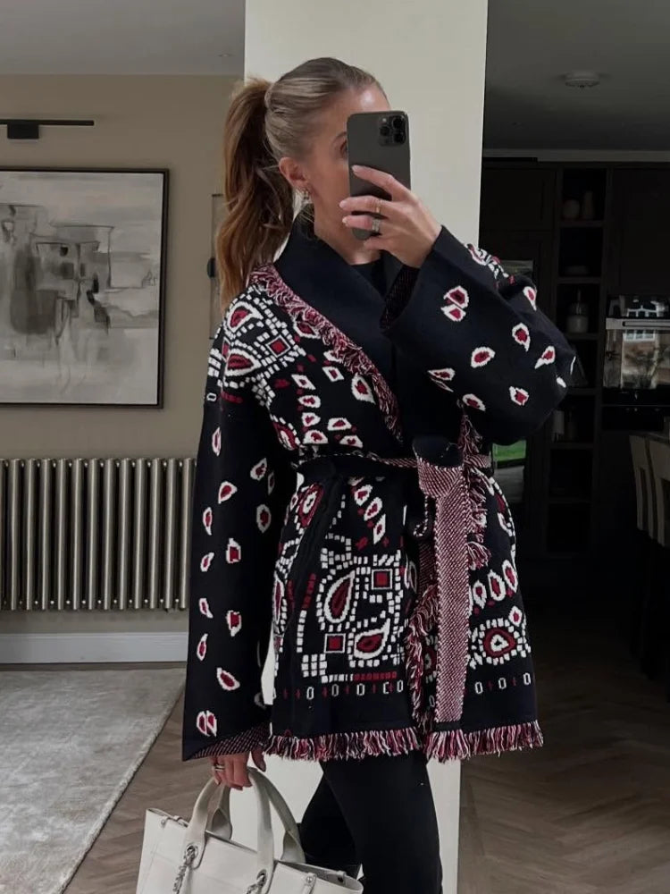 Woman taking a mirror selfie wearing a patterned black and pink coat in a room.