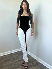A woman wearing a black and white evening dress for an upscale formal event is standing against a plain wall.