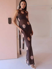 Woman wearing a brown dress with pink polka dots in a minimal indoor setting.