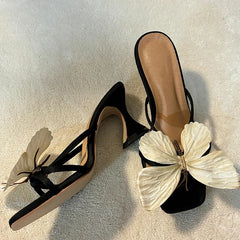 Black high-heeled sandals with white butterfly decorations on a light background