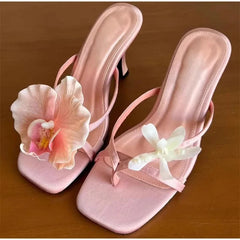 Pink high-heeled sandals with floral decorations on a brown surface