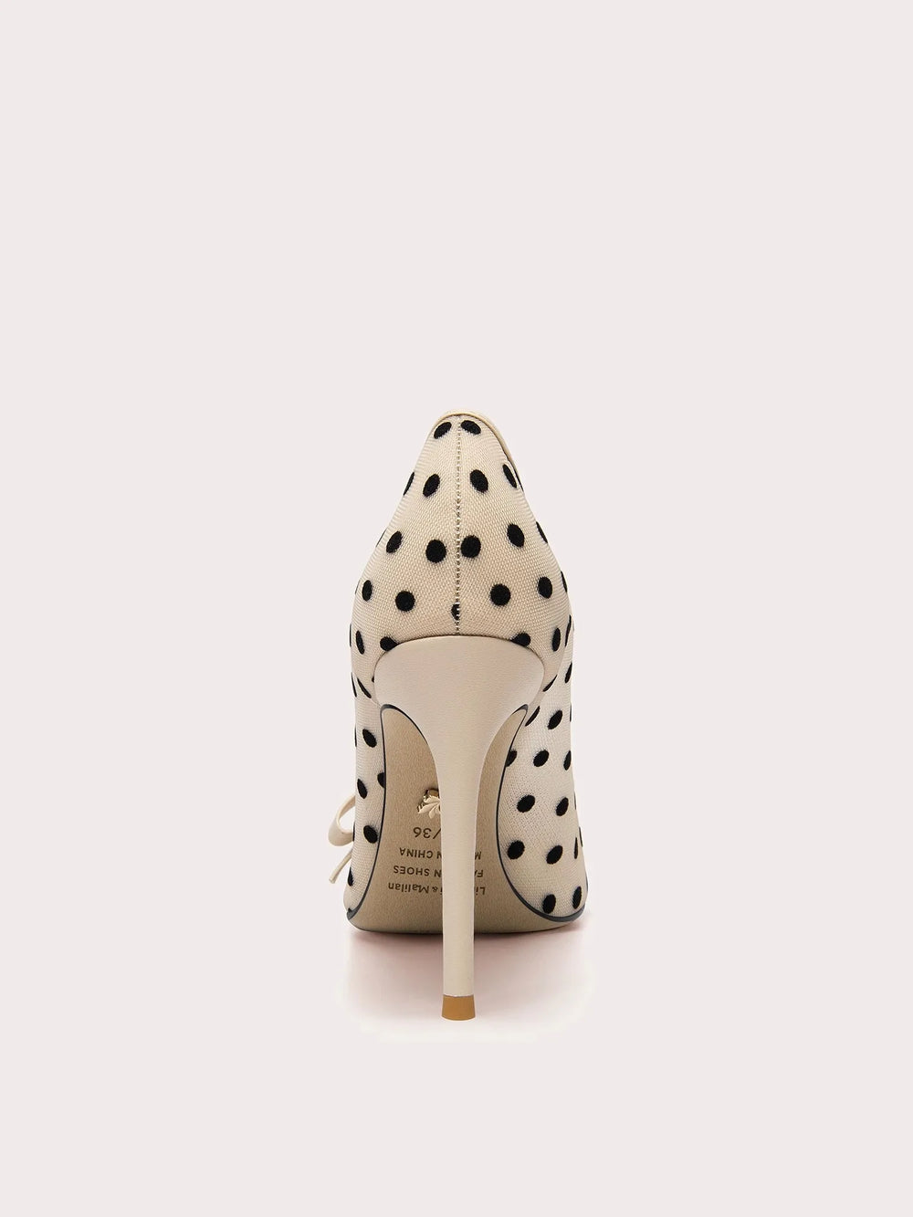 White high-heeled shoe with black polka dots on a white background