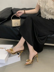 Person wearing gold high-heeled shoes and holding a small handbag on a gray floor.