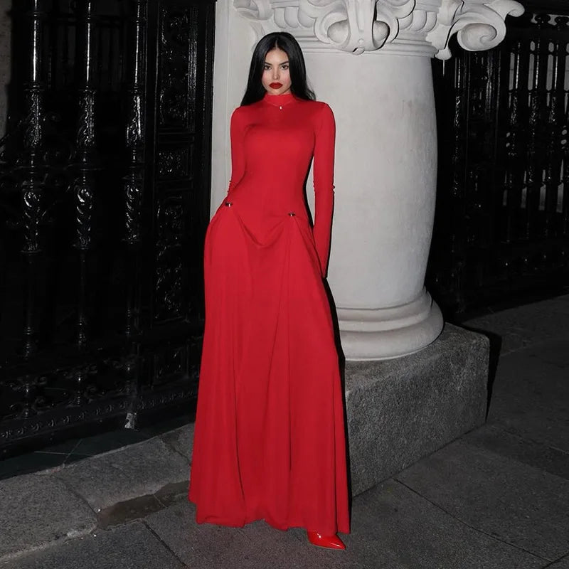 Woman in a elegant red long sleeve maxi dress styled for formal evening parties  standing against a dark background
